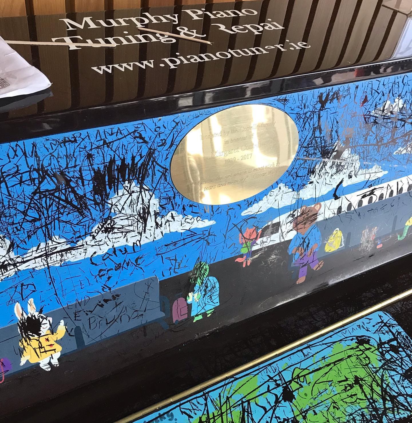 A blue illustrated public piano beneath a mirror in Dublin Airport